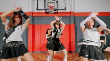 A group of dancers performing in a gymnasium, wearing stylish outfits with black skirts and white tops. They are in dynamic poses, showcasing their choreography. video
