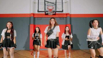A group of dancers performing in a gymnasium, wearing stylish outfits with black skirts and striped tops. The energetic dance routine showcases their synchronized movements and enthusiasm. video