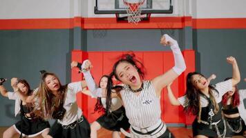 A dynamic dance performance featuring a group of five young women in stylish outfits, showcasing energetic movements in a gymnasium setting with red and gray walls. video