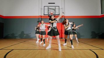 A group of dancers performing in a basketball court, showcasing synchronized movements in stylish outfits. The background features a basketball hoop and a wooden floor. video