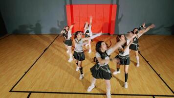 A group of young dancers performing a choreographed routine in a gymnasium. They are dressed in matching outfits, showcasing energetic movements against a basketball court backdrop. video