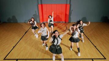 A dynamic dance performance by a group of young women in a gymnasium. They wear matching outfits and showcase synchronized movements, with a basketball hoop in the background. video