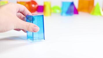 A hand interacts with colorful 3D geometric shapes on a white surface, highlighting educational and playful elements video