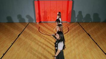 A group of five dancers standing in a gymnasium, with shadows cast on the wooden floor. They are dressed in stylish outfits, showcasing a dynamic pose video