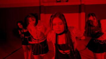 A group of girls in a gymnasium, illuminated by red lighting, creating a dramatic atmosphere. They appear to be engaged in a dance or performance, with dynamic movements. video