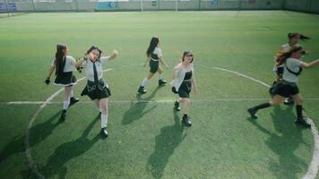 A group of six young women performing a dance routine on a sports field. They are dressed in stylish outfits, with a mix of skirts and tops, showcasing energetic movements video