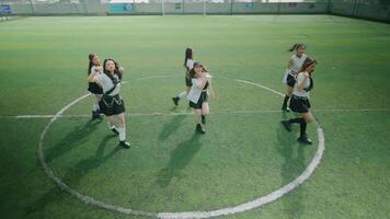 A group of six dancers performing on a green turf field, showcasing synchronized movements. They are dressed in stylish outfits, with a lively and energetic atmosphere. video