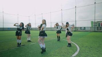 A group of six dancers performing on a soccer field, dressed in stylish black and white outfits. They are showcasing synchronized movements with a lively atmosphere. video