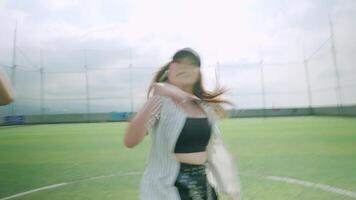 A dynamic dance performance on a sports field, featuring a female dancer in a baseball cap and crop top, with two other dancers in the background. The scene captures energy and movement video