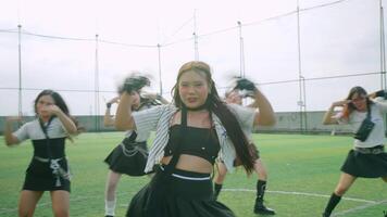 A group of dancers performing on a sports field, showcasing energetic choreography. The lead dancer, wearing a black crop top and a striped jacket, stands out with expressive movements video