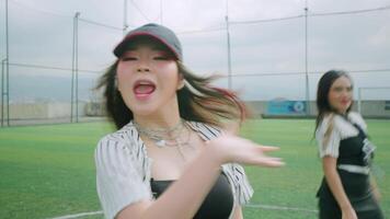 A dynamic scene on a sports field featuring two dancers in stylish outfits. One dancer is in the foreground, energetically performing with a confident expression video