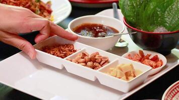 Hands arranging ingredients for Miang Kham on a tray. Bright lighting highlights vibrant colors and textures in a Thai culinary setting video