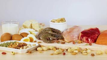A variety of protein-rich foods including meats, nuts, and dairy are neatly arranged on a table in bright lighting video