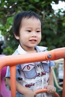 Close-up portrait of smiling boy having fun climbing toys in playground, 2 year old Asian child with enthusiasm, muscle development. photo