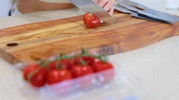A person slices tomatoes on a wooden cutting board in a bright kitchen setting video