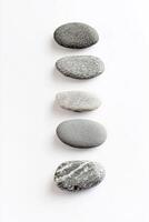 A simple top down view of five smooth gray stones stacked vertically on a white surface photo