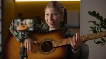 Creative little girl blogger Caucasian teaching how to play guitar record mobile phone camera tripod learning playing music influencer child kid filming tutorial song musical instrument at home photo