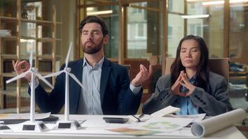 Multiethnic relaxed business team meditating wind turbine startup windmill models eco engineers Korean woman Caucasian man stress relief sustainable energy green focus harmony innovation peaceful rest photo