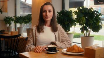 Caucasian woman visitor in cafe business lady calm relaxed girl female at cafeteria table relaxing with coffee and croissant looking at camera portrait customer order service enjoying coffeehouse photo