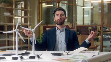 Engineer meditating business wind turbine project models stress relief green startup renewable energy design focus Caucasian man male peaceful businessman mindfulness sustainable innovation at office photo