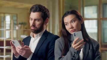 Multiethnic office workers Korean businesswoman Caucasian businessman using mobile phone business coworkers glancing colleagues screen curiosity distraction privacy cellphone online work internet app photo
