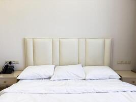 A white bed with white pillows and a phone on the nightstand photo