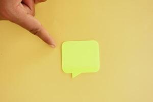 Hand pointing at green sticky note on yellow background photo