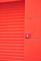 Bright red wall with closed rolling door and number label photo