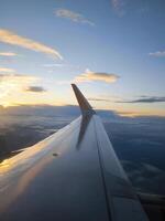 Wing of an airplane flying above clouds against the backdrop of a sunset. Flight on an airplane. photo