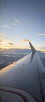 Wing of an airplane flying above clouds against the backdrop of a sunset. View from the airplane window. photo