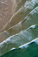 overhead perspective of layered sea waves and sand patterns along the coast photo