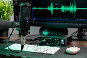 Black studio microphone on a desk with a computer monitor showing a green audio waveform, perfect for podcasting, music production, and content creation photo