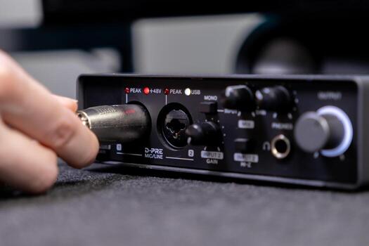 A hand expertly connects an XLR audio cable into the D-PRE MICLINE input of a compact black sound interface, demonstrating professional setup for high-fidelity recording or live streaming photo