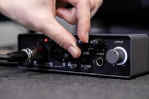 Close-up of person's hand turning a knob on professional audio interface, actively controlling sound settings for music production or podcast recording sessions photo