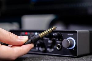 Human hand holds a golden audio jack, poised for connection into a professional sound amplifier, symbolizing music production and home studio setup photo