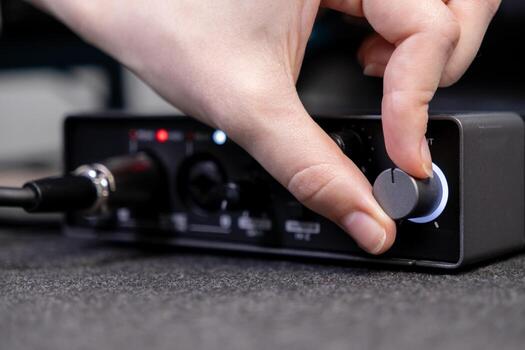 A human hand precisely adjusts the illuminated control knob on a professional audio interface, signifying sound engineering and music production for digital media creation photo