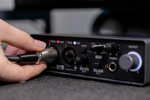 Close-up of a hand inserting an XLR microphone cable into a professional audio interface, highlighting input gain and USB indicators for home studio recording photo