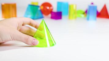 A hand interacts with vibrant 3D geometric shapes on a white surface under bright lighting, highlighting educational play video