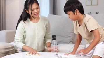 A mother and son clean a table in a bright living room, sharing smiles and teamwork video