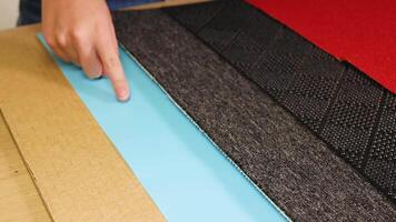 A hand examines different textured surfaces including cardboard, plastic, rubber, and carpet under bright lighting video