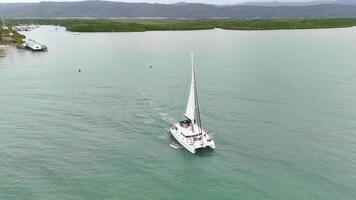 Drone captures a catamaran sailing smoothly in calm, turquoise waters under overcast skies video