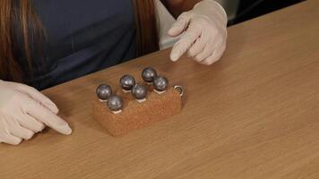 Gloved hands manipulate metal spheres on a cork block. Neutral lighting, close-up focus, and steady camera capture the detailed process video