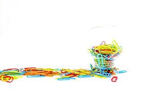 A vibrant collection of colorful paper clips spilled around a container on white background photo