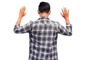 Rear view of a young Asian man with hands raised in surrender on white background. Depicting surrender photo