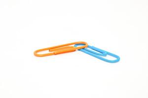Two colorful paper clips, one orange and one blue, intertwined on white surface, minimal photo