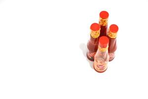 Lampung, July 03, 2025, A cluster of red-capped chili sauce bottles arranged on a plain white surface, isolated shot photo