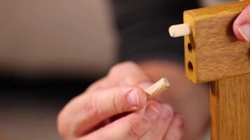 Hands insert dowels into wooden furniture joints under soft lighting, demonstrating precise craftsmanship and assembly techniques video