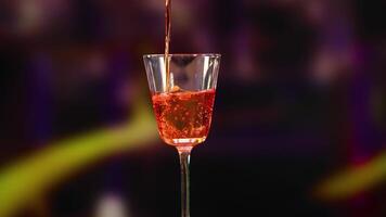 A Negroni cocktail is poured and garnished with an orange peel in a dimly lit setting video