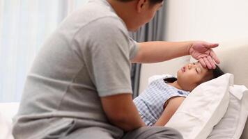 A father checks his daughter's temperature as she lies in bed, conveying care and concern in a softly lit room video