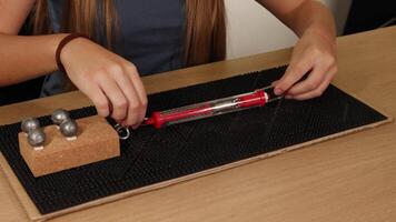 Hands use a spring scale to measure force needed to drag weights on a cardboard surface, illustrating friction principles video